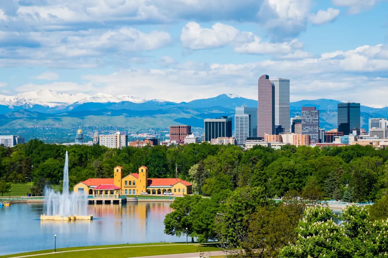 Denver skyline with a lake, fountain, and mountains visible in the background.
