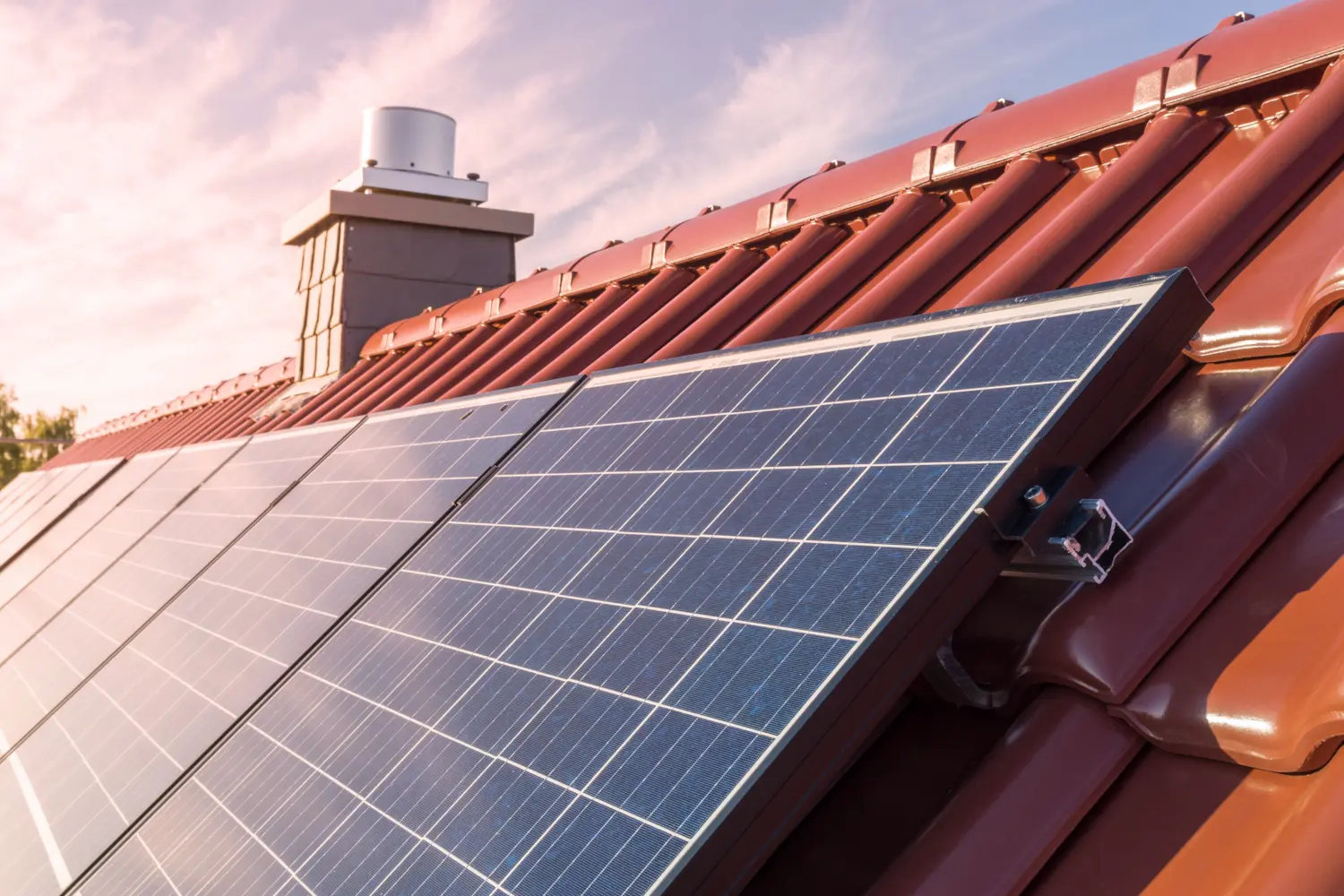 Close-up of solar panels mounted on a red tile roof at sunset.