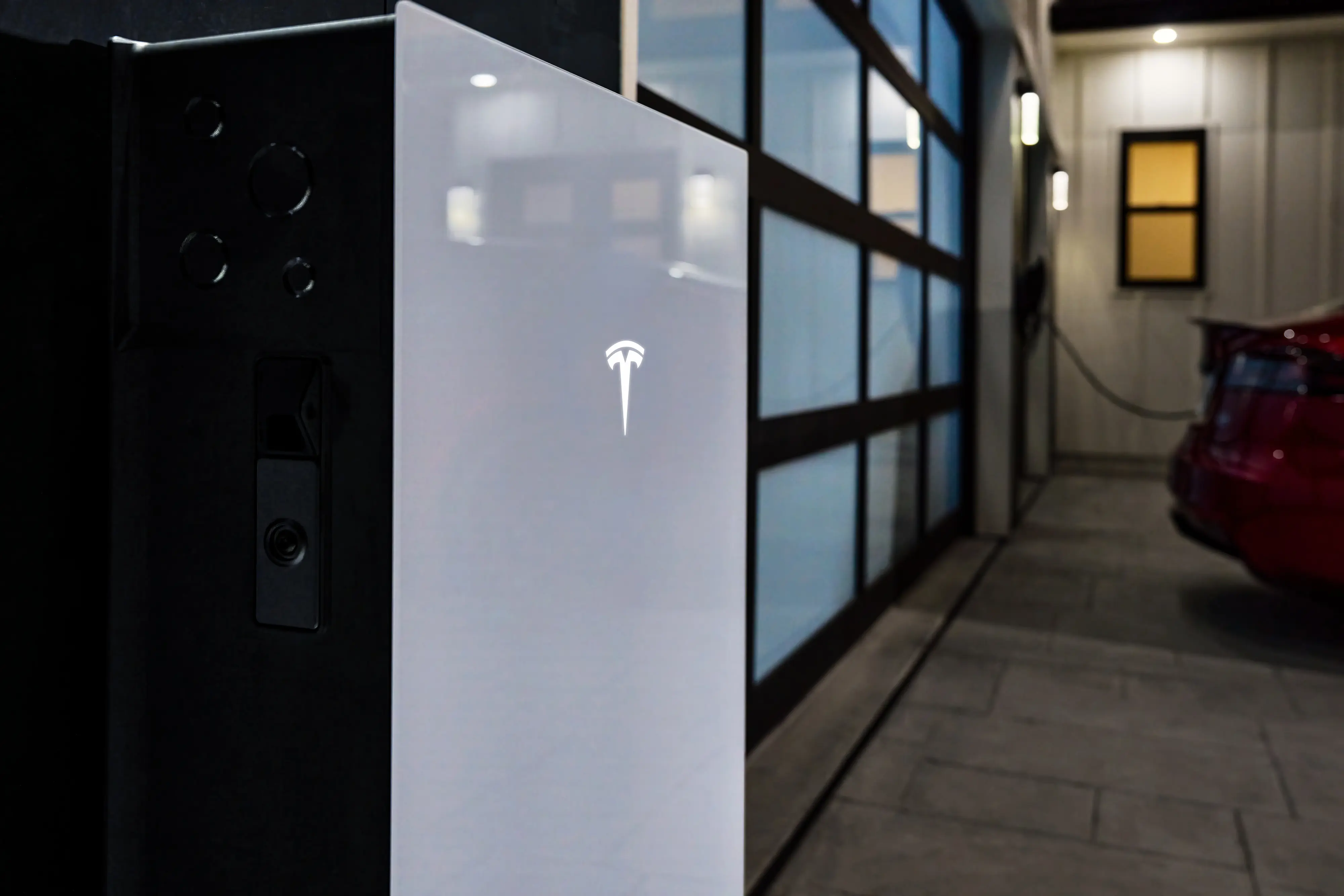 Tesla Powerwall 3 installed in a residential garage with a Tesla vehicle charging nearby at night.