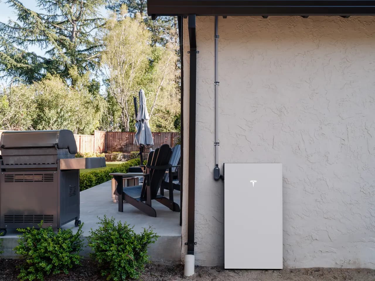 Tesla Powerwall 3 with integrated inverter mounted on an exterior wall near a backyard patio