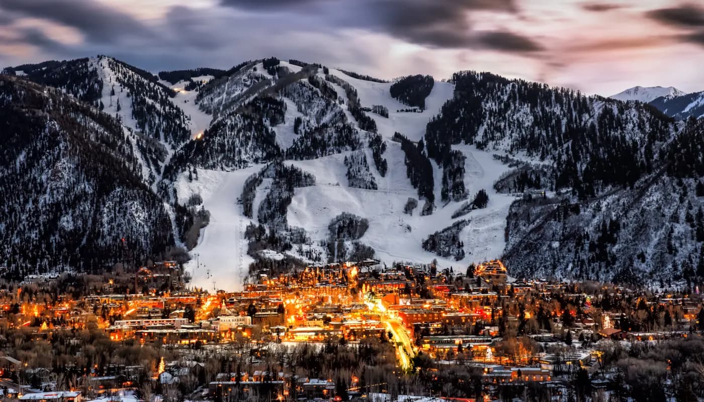 Nighttime view of Aspen’s illuminated mountain town and snowy ski slopes in Colorado.