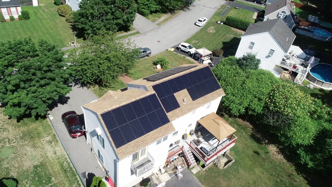 Rooftop solar panels on a light-colored New England-style home with autumn foliage in the background.