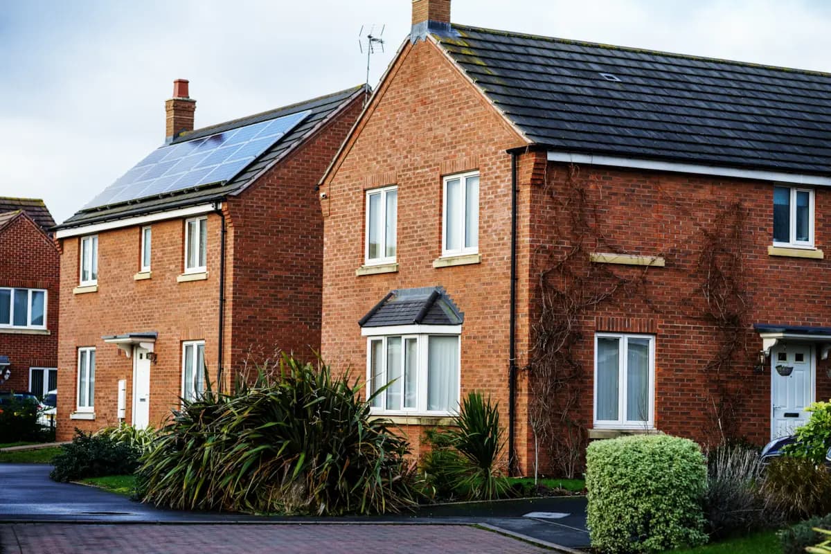 Row of red brick homes with rooftop solar panels in a suburban neighborhood.