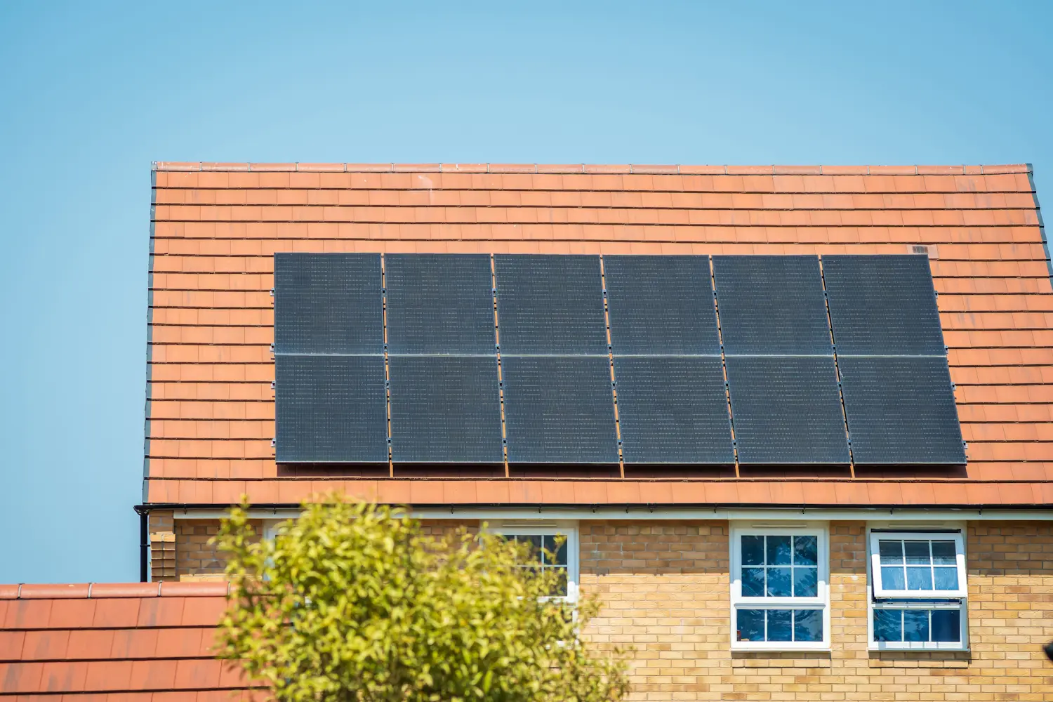Close-up of black solar panels mounted on an orange tile roof under a clear blue sky.