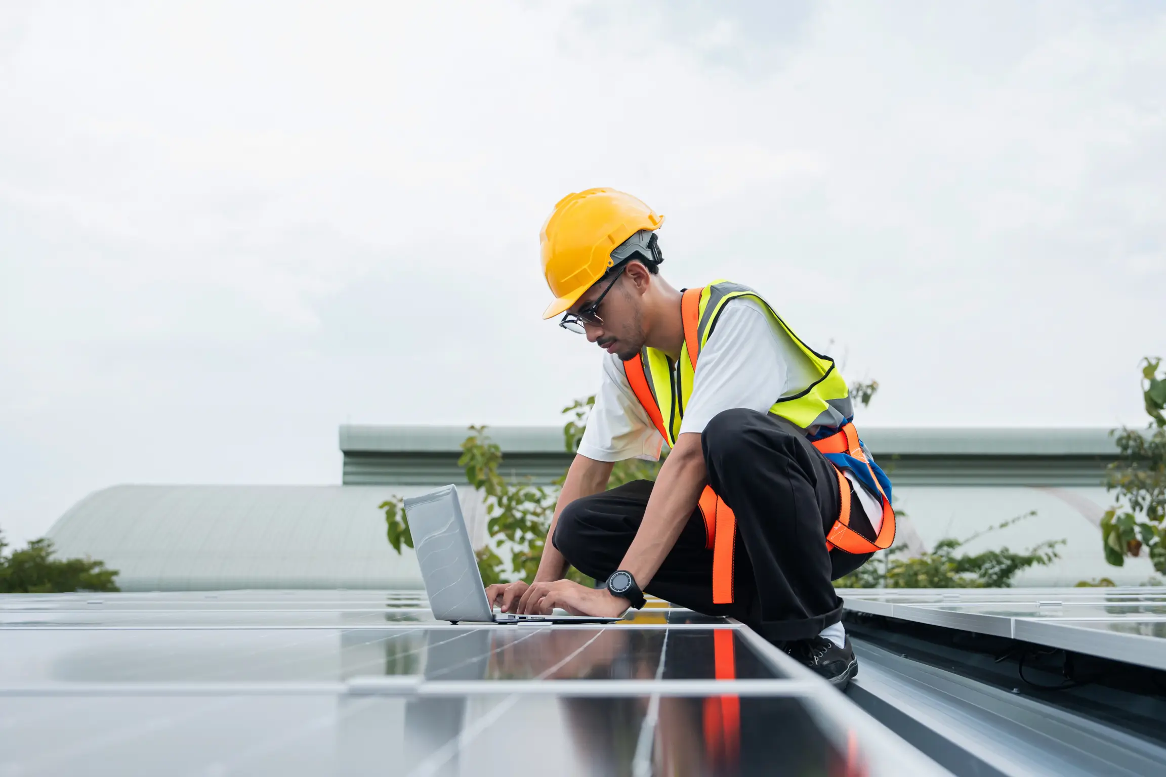 Solar technician using a laptop to check performance data on a rooftop solar panel system.