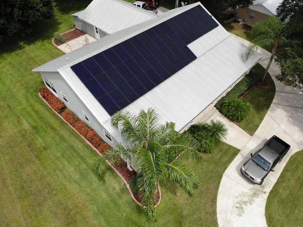 Lunex rooftop solar system on a white metal roof with red flowering plants below.