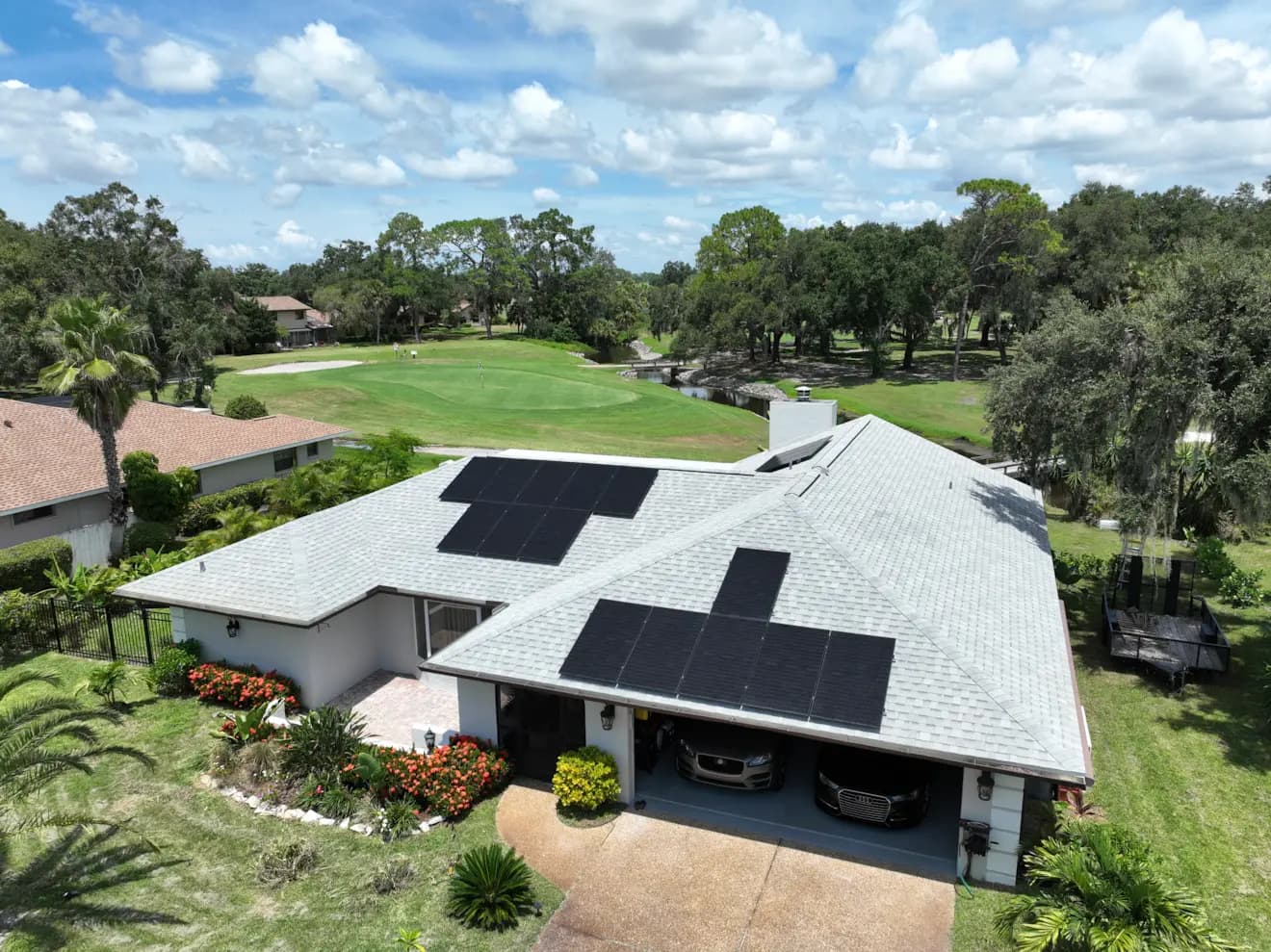 Aerial view of a home with rooftop solar panels overlooking a green golf course.